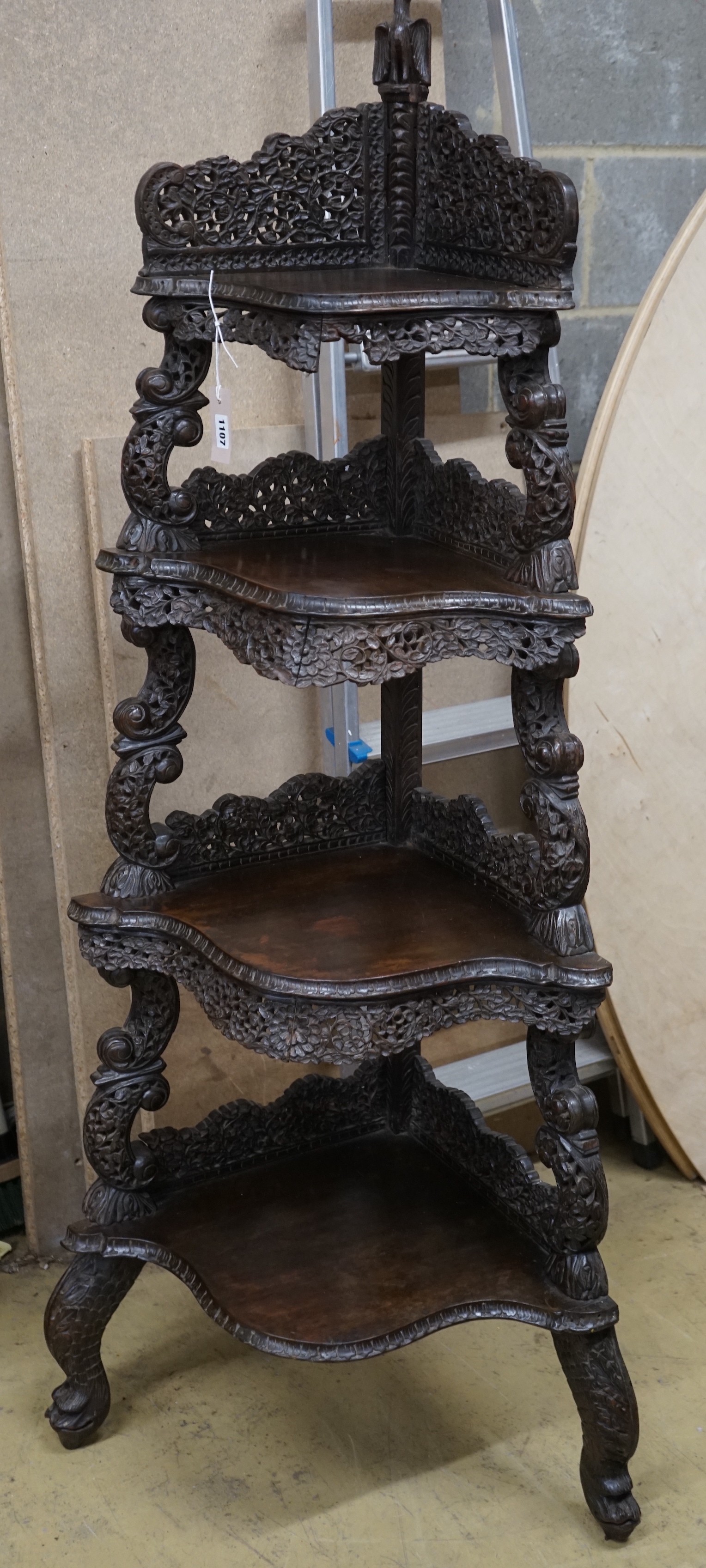 A 19th century Burmese carved hardwood serpentine corner whatnot, width 60cm, depth 42cm, height 153cm